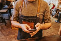 Mid section of man dressed in jeans apron using smartphone. — Stock Photo