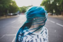 Portrait of girl posing with face covered with locks of blue hair at street scene — Stock Photo