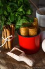 Close up view of fried honey dough with mint in mug near wooden scoop and cinnamon sticks on white wooden table — Stock Photo