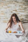 Girl holding tray with breakfast in bed — Stock Photo
