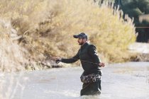 Вид сбоку человека, стоящего в воде и рыбачащего с удочкой — стоковое фото