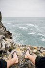 Crop homem descalço sentado na costa rochosa — Fotografia de Stock