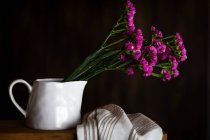 Claveles morados frescos en taza sobre fondo oscuro con toalla de cocina - foto de stock