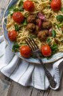Спагетті і фрикадельки прикрашені листям базиліка і смаженими помідорами на тарілці — стокове фото
