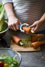 Midsection of woman peeling carrot with vegetable peeler — Stock Photo
