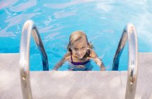 Blonde kid in swimming pool by ladder — Stock Photo