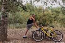 Вид збоку літнього чоловіка, що розтягує ноги в парку біля велосипеда — стокове фото