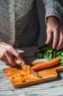 Crop image of frmale hands slicing carrot on woden board — Stock Photo