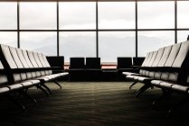 Asientos vacíos en los salones del aeropuerto contra grandes ventanales . - foto de stock