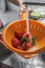 Nahaufnahme menschlicher Hände beim Waschen frischer Erdbeeren im Sieb — Stockfoto