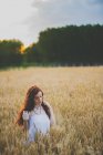 Портрет рудої волохатої дівчини в білій сукні, що позує на життєвому полі під час заходу сонця — стокове фото