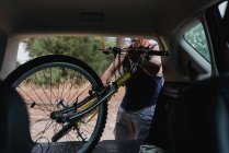 Homem sênior colocando bicicleta no porta-malas do carro no campo — Fotografia de Stock