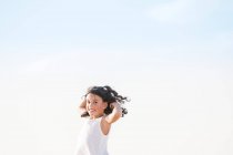 Portrait of cheerful brunette kid with toothy smile and flying hair against blue sky. — Stock Photo