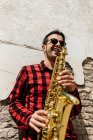 Mann lehnt sich an Wand und spielt Saxofon — Stockfoto