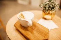 Close up view of cup of cappuccino on wooden board on table with plant — Stock Photo