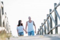 Couple holding hands and walking on wooden boardwalk — Stock Photo