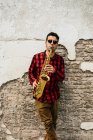 Jazzman appoggiato al muro di mattoni e suonare il sax — Foto stock