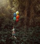 Mujer joven con globos de colores caminando en el bosque silencioso . - foto de stock