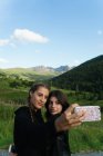 Les jeunes femmes debout sur la prairie ensemble et prendre selfie avec smartphone . — Photo de stock