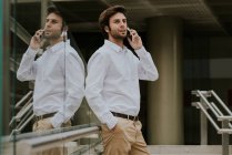Скляний паркан, що відображає брюнетку бізнесмен у білій сорочці, розмовляє на смартфоні на міській сцені — стокове фото