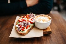 Close up view of wooden board with cup of cappuccino and toast with fruits and cream — Stock Photo