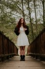 Веселая девушка в белом платье позирует на деревянном мосту — стоковое фото