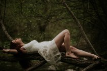 Чувственная девушка в белом платье лежит на ветке дерева — стоковое фото