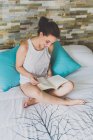 Mädchen sitzt auf dem Bett und liest Buch — Stockfoto