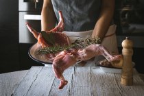 Primo piano della donna che tiene la carcassa di coniglio crudo con ingredienti sul tavolo di legno — Foto stock