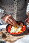 Mid section putting ingredient in pan with scrambled eggs and dried tomatoes — Stock Photo