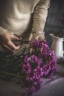 Close up view of female florist hands cutting with scissors bouquet of flowers on table — Stock Photo