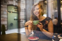 View through window to woman having coffee alone at cafeteria — Stock Photo