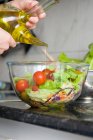 Crop hands adding olive oil to bowl of salad — Stock Photo