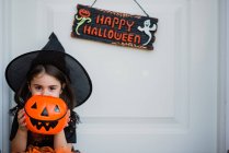 Girl in witch costume hiding face with pumpkin bag — Stock Photo