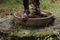 Cropped image of male legs in stylish boots standing on moss covered sewer manhole — Stock Photo