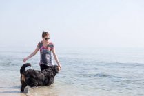 Femme heureuse jouant avec chien sur la plage — Photo de stock