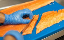 Mano maschile in guanti sta tagliando salmone fresco su fette . — Foto stock