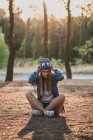 Ritratto di donna seduta a terra nella foresta e che regola divertente cappello di lana — Foto stock