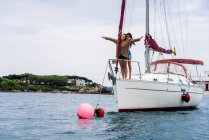 Young embracing girls standing on nose of yacht over green shoreline — Stock Photo