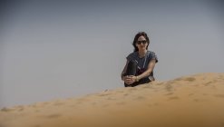 Женщина, сидящая на песке и смотрящая в камеру — стоковое фото