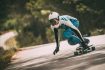 Unrecognizable man in blue suit and helmet riding fast on skateboard — Stock Photo