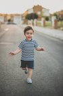 Netter Junge in kurzen Hosen rennt fröhlich auf der Straße in Richtung Kamera. — Stockfoto