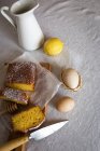 High angle view of lemon cake slices on board over table with ingredients on rumpled tablecloth — Stock Photo