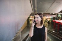 Ritratto di giovane donna che si muove sulla scala mobile e parla su smartphone alla stazione ferroviaria — Foto stock