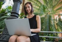 Low angle portrait of smiling girl sitting and using laptop on knees — Stock Photo