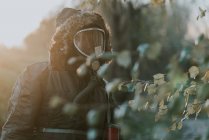 Portrait of man wearing coat hood and gas mask walking in countryside field — Stock Photo