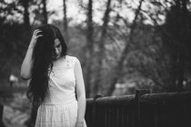 Чуттєва дівчина в білій сукні дивиться вниз і торкається волосся на природі — стокове фото