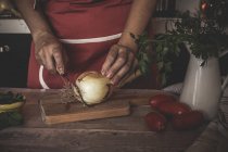 Coltivare le mani affettare la cipolla su tavola di legno — Foto stock