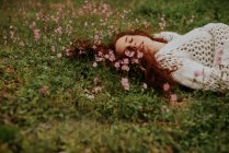 Мечтательная девушка с закрытыми глазами лежит на земле с цветком — стоковое фото