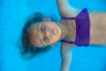 Porträt eines Kindes, das im Pool mit türkisfarbenem Wasser schwimmt — Stockfoto